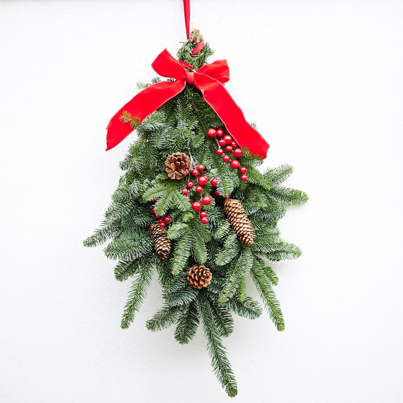 Noblis fir  branches, a large red ribbon bow at the top, red berries, and  pinecones.